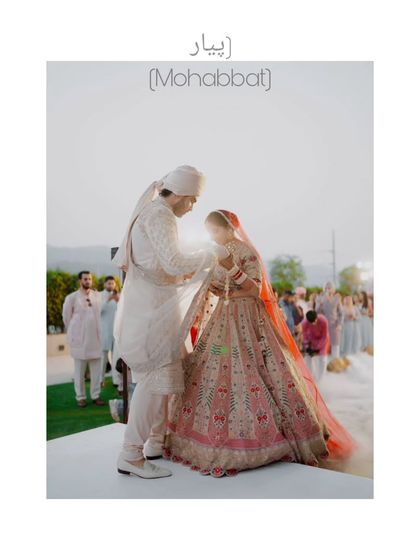 A beautiful wide shot of the varmala (garland exchange) ceremony, capturing the couple against a soft, bright background. The word "Mohabbat" (love) perfectly describes the moment.
