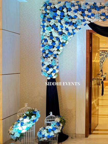 A close-up of the blue and white floral entrance arch, showing the detail of the flower arrangements and the charming pigeon cage accent.