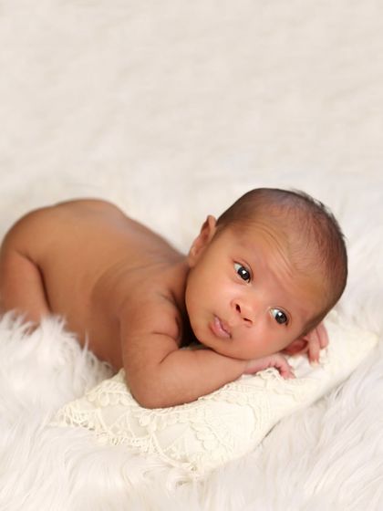 An awake and curious newborn enjoying some tummy time on a soft pillow. This pose is great for capturing their strength and those beautiful, wide-eyed expressions.