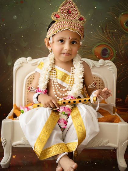 A handsome little boy dressed as Lord Krishna for Janmashtami. The detailed costume, complete with a crown and flute, is provided by my studio.