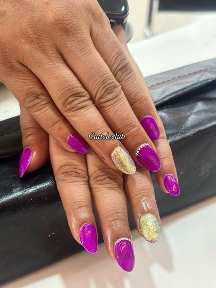 A vibrant purple and gold combination. The cat-eye effect on the gold nails creates a beautiful shimmer, complemented by the glossy purple and rhinestone details.