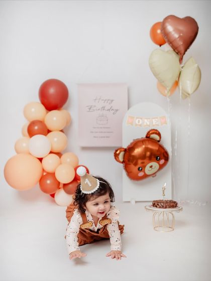 A wide view of the adorable teddy bear first birthday setup, featuring balloons, a "Happy Birthday" banner, and a tiny cake just for her.