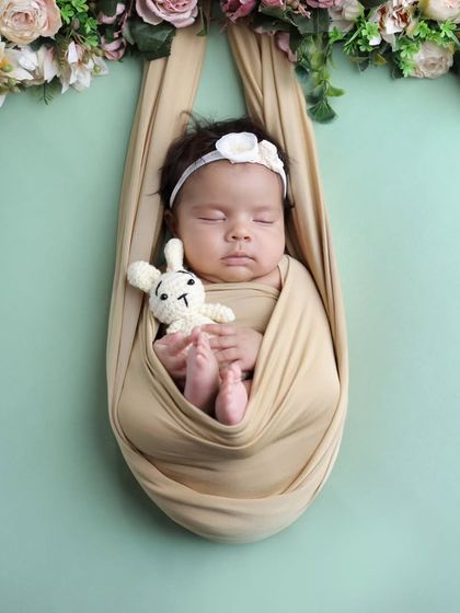A hanging floral sling pose. The baby is safely and comfortably nestled in a sling adorned with a beautiful floral garland, creating a stunning and artistic portrait.