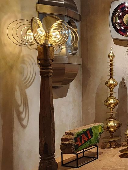 Curated objects from the 'Indofuturism' installation, blending traditional Indian forms with retro-futuristic aesthetics. A lamp made from a reclaimed wooden pillar stands next to brass objects, creating a kitschy yet sophisticated decor that complements the theme.