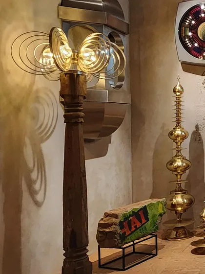 A curated collection of kitschy and retro-futuristic decor objects from the 'Indofuturism' installation. The juxtaposition of a traditional wooden pillar with a modern lamp creates a unique hybrid aesthetic.