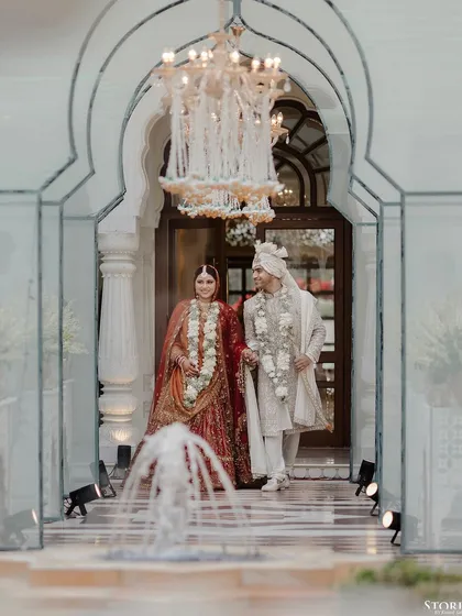 The couple, Shikha and Rupen, walking out of the palace doors after their ceremony, framed by a fountain.