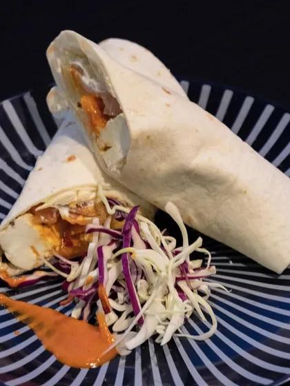 A delicious and satisfying chicken shawarma wrap, served with a side of fresh coleslaw and a drizzle of spicy sauce.