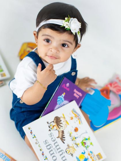 This little book lover is ready for story time, holding her books in a cute school-themed setup.
