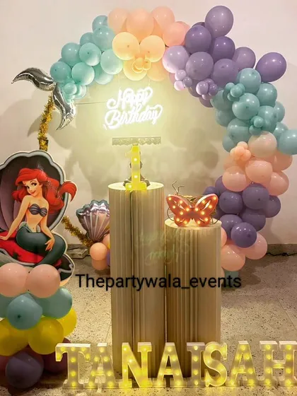 A mermaid theme with a neon "Happy Birthday" sign. The pastel balloon arch and Ariel cutout in a seashell look magical with the glowing light.