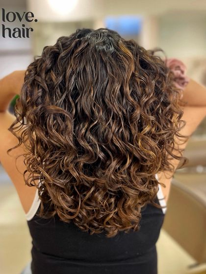 Lush, hydrated curls with a touch of balayage. This client's curly bob is enhanced with subtle highlights for a rich, dimensional brunette look.