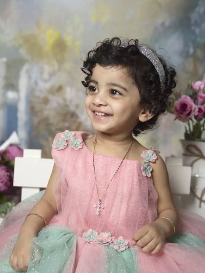 A beautiful portrait of a toddler in a pink and green tulle dress, set against a whimsical, painted garden backdrop.
