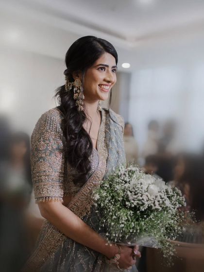 The bride smiles as she holds a bouquet of white flowers. This candid shot captures her happiness and the delicate details of her engagement look.