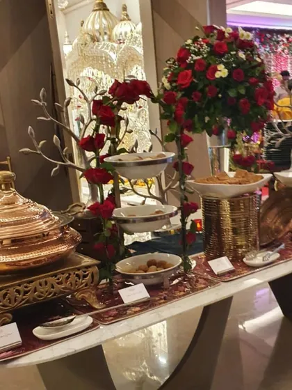 A lavish buffet table decorated with stunning red rose centerpieces and silver tree accents. The combination of copper serveware and rich floral decor is perfect for a luxurious wedding reception.