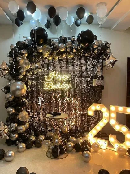 This black and silver themed birthday decor is perfect for a chic and glamorous party. The centerpiece is a floor-to-ceiling shimmer wall that catches the light beautifully, complemented by a balloon arrangement, a 'Happy Birthday' neon sign, and light-up marquee numbers.
