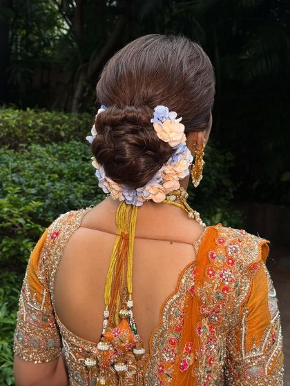 A view of the beautiful bridal bun, adorned with delicate pastel flowers that contrast beautifully with the warm tones of the lehenga.