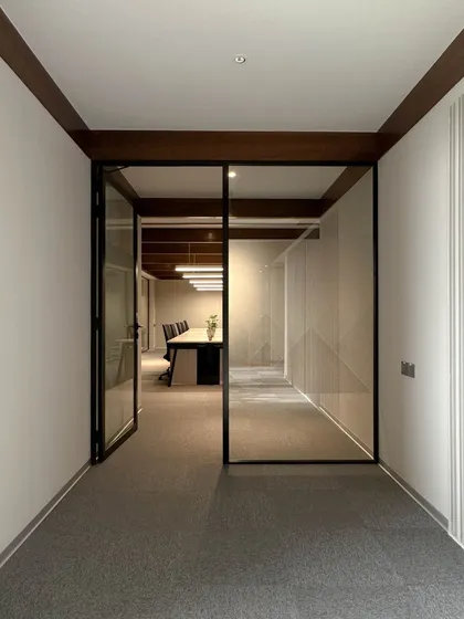 A view from a connecting corridor into a glass-enclosed conference room. The use of full-height glass partitions promotes a sense of transparency and openness while maintaining acoustic privacy for meetings.