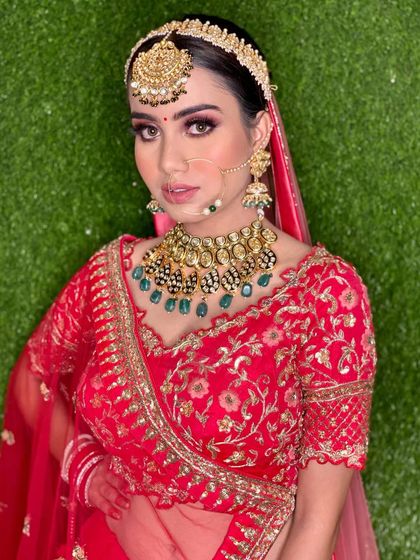 The full bridal look against a green backdrop. The contrast makes her red lehenga and intricate jewelry stand out even more.
