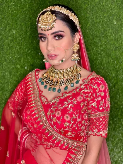 The full bridal look against a green backdrop. The contrast makes her red lehenga and intricate jewelry stand out even more.
