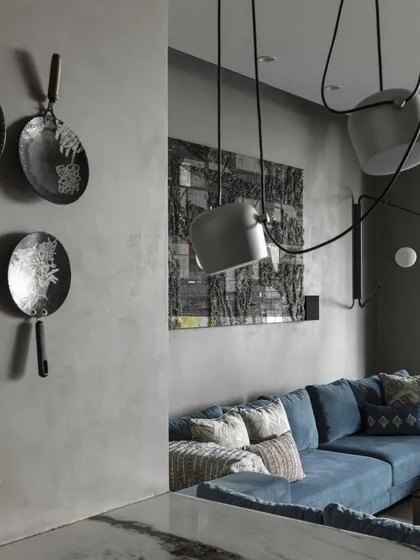 The first-floor family lounge at the Bammi Residence, a cozy retreat with grey concrete-finished walls. The space features a custom blue sofa, whimsical art pieces, and a modern Flos light installation.