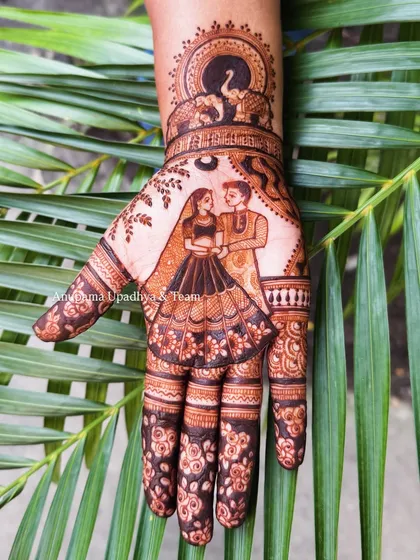 This Karwa Chauth design features a sweet couple portrait on the palm, with elephants under a sun motif on the wrist, symbolizing strength and good fortune.