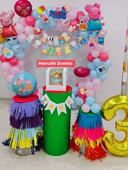A sweet Peppa Pig party with a circular balloon arch and colorful fringed plinths. The setup includes a large number "3" balloon and a spot for the cake.