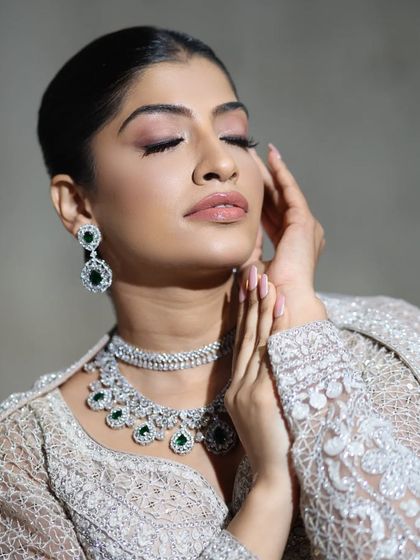 A serene and elegant pose, this close-up highlights the beauty of the emerald and zircon necklace against the delicate white outfit.