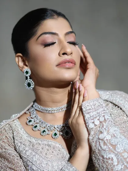 A serene and elegant portrait. The model's eyes are closed, drawing attention to the stunning emerald and zircon layered necklace that adorns her, perfect for a sophisticated evening affair.
