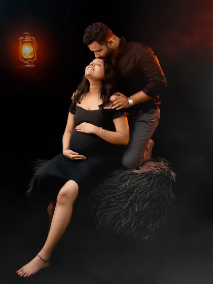 A dramatic and romantic couple portrait. Lit by the warm glow of a lantern, the partner kisses the mom-to-be's forehead in this intimate and moody shot.