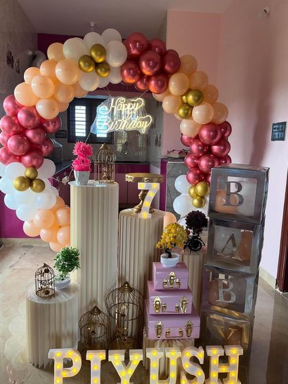 A colorful and festive birthday setup with multiple plinths and props. The decoration includes a balloon arch, marquee letters, and decorative birdcages.