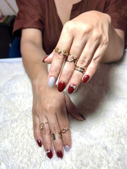 A glamorous set with a mix of solid red and a silver glitter accent nail adorned with a rhinestone bow.