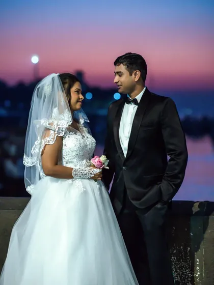 A romantic evening shot of a couple dressed for their wedding, looking at each other against a colorful sky.