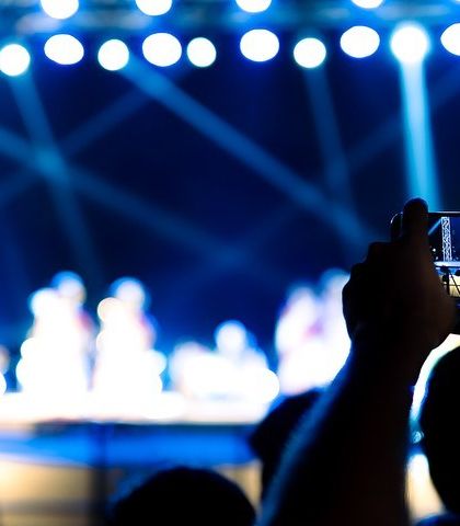 A close-up of a phone screen recording the performance, with the stage beautifully blurred in the background. This image highlights the technology we use to capture our favorite moments.
