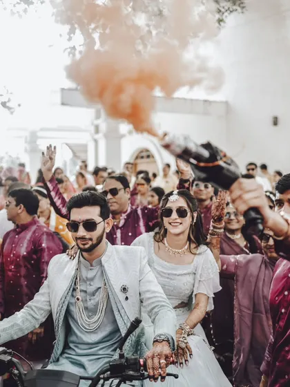 A fun and modern baraat entry! The couple makes their way through the cheering crowd on a scooter, complete with a colored smoke bomb for that extra bit of flair.