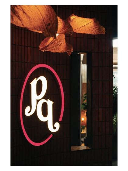 The glowing 'pq' logo for Prequel, set against a dark, textured wall. This simple yet effective branding element serves as a beacon, guiding guests into the space.