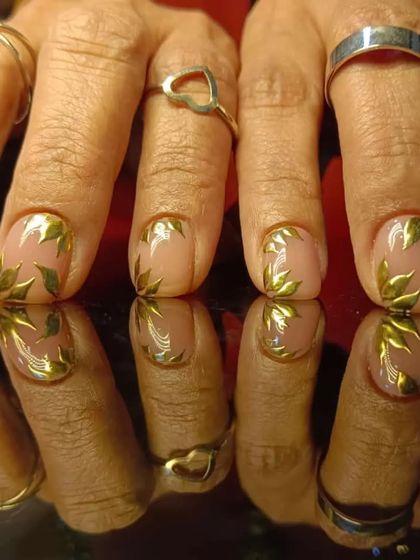 A full view of the metallic leaf pattern nails, styled with silver rings.