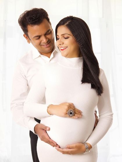 A lovely, light-filled maternity portrait. The expecting parents share a happy moment, and their white outfits contribute to the bright and airy feel of the photo.