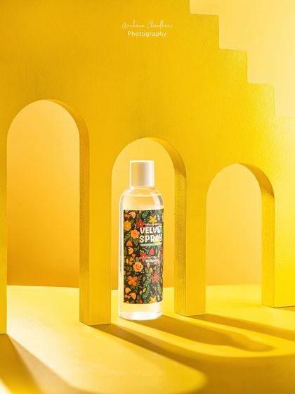 A creative shot of a floral body spray using custom-painted yellow arches as props. This architectural setup creates a unique and modern look that makes the product stand out.