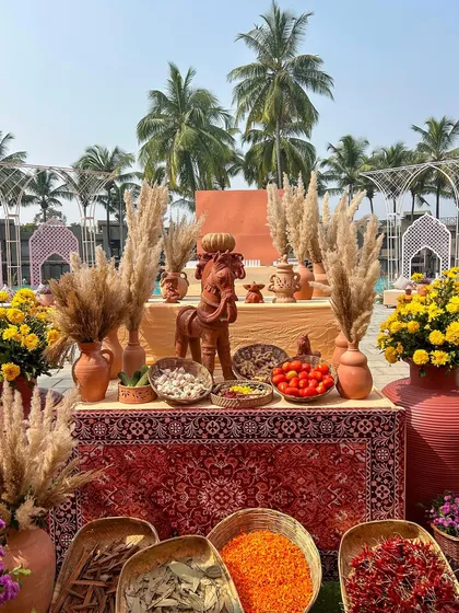 A detailed shot of our 'Souk Bazaar' Haldi theme, featuring terracotta pots, pampas grass, and bowls of spices and flowers on a rich Persian rug, creating an authentic market feel.