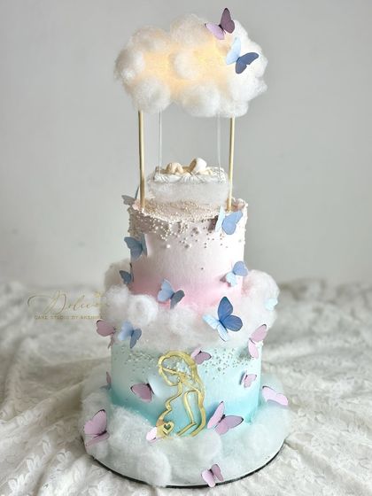 A dreamy, multi-tiered baby shower cake with a floating cloud and swing. This design combines structural techniques with soft textures like cotton candy clouds.