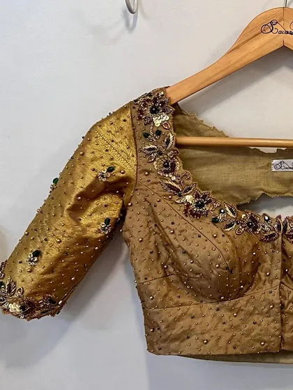 A classic gold Kanjeevaram bridal blouse, elevated with hints of green beads and intricate floral embroidery around the neckline and back cutout.
