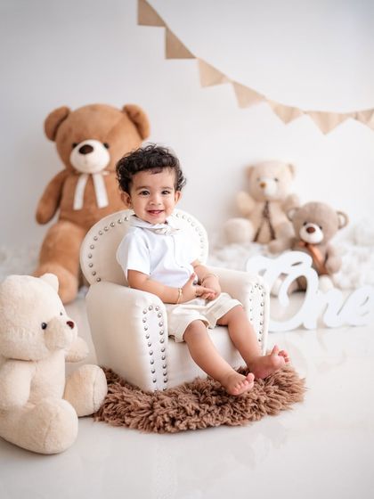 A classic first birthday setup with teddy bears and a "ONE" sign. This little boy looks so happy in his mini armchair.