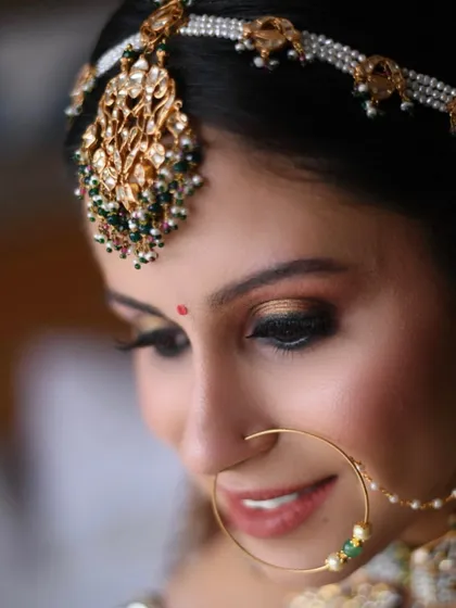 A close-up showcasing the artistry of a classic bridal makeup look. This features a warm, golden smokey eye, perfectly defined brows, and a soft nude lip, all framed by an ornate matha patti and nath for a traditional yet elegant feel.
