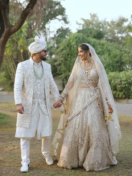 An elegant outdoor wedding portrait of a couple in beautiful white traditional attire, walking hand-in-hand.