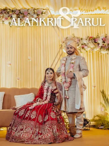 A classic stage portrait of Alankrit and Parul, seated together, their red and beige outfits creating a timeless and elegant look.