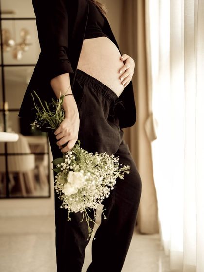 An artistic indoor shot focusing on the baby bump, with the mom-to-be holding a bouquet of baby's breath. The composition is elegant and minimalist.