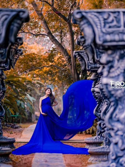 A beautiful maternity shot framed by ornate stone pillars, with the autumn-colored leaves in the background adding a warm touch.