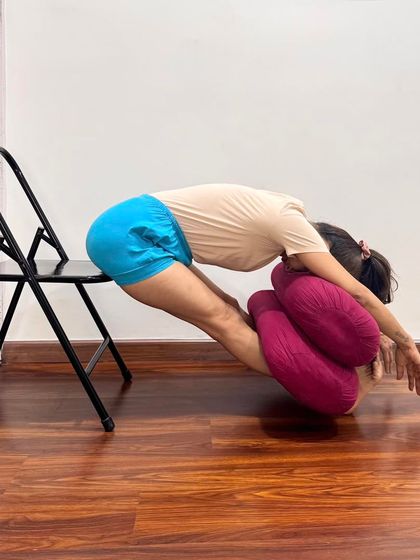 A supported forward bend using a chair and bolsters. The key is to maintain a straight spine to keep the brain alert, ensuring a thorough communication between the organs of action and senses of perception.