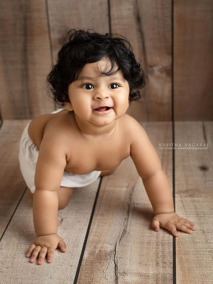Eight-month-old Viaan on the move. The simple wooden backdrop and white diaper cover keep the focus on his adorable crawling pose and happy face.