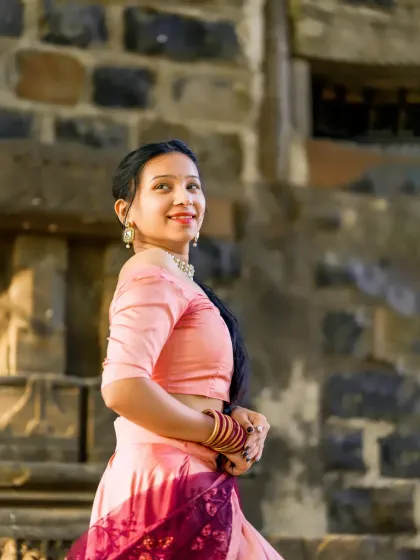 A classic portrait pose, capturing the model's graceful turn and smile in her traditional pink lehenga.