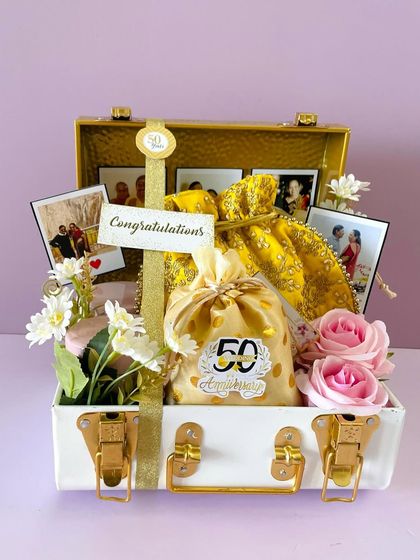 A beautiful dry fruits hamper for a 50th Anniversary celebration. The white and gold trunk is filled with decorative potlis and personalized with photos.